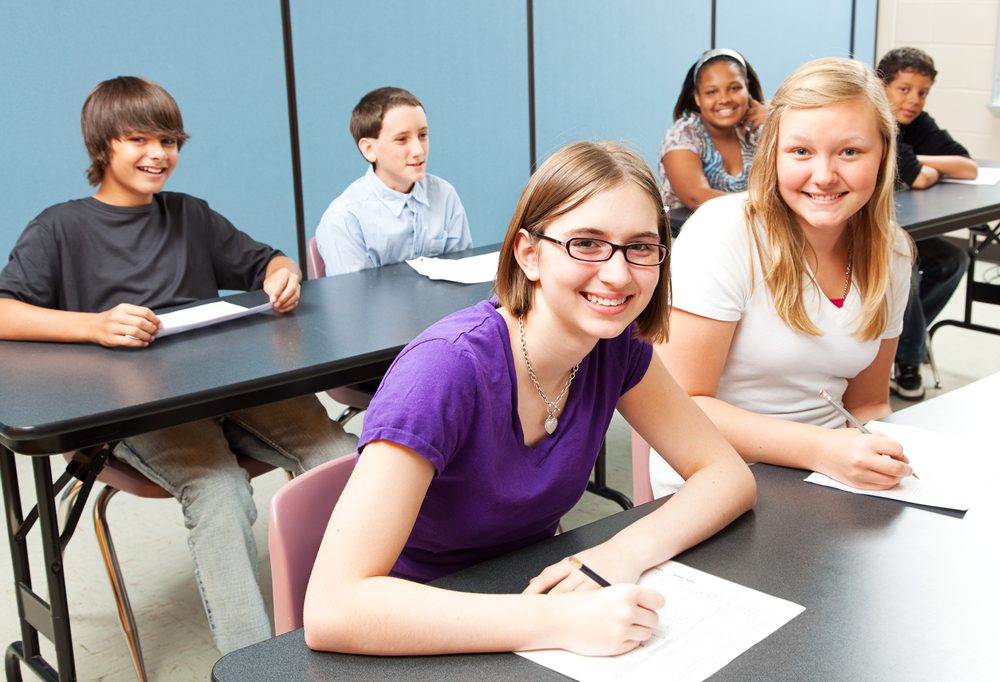 Children in Middle School are smiling and writing on a paper