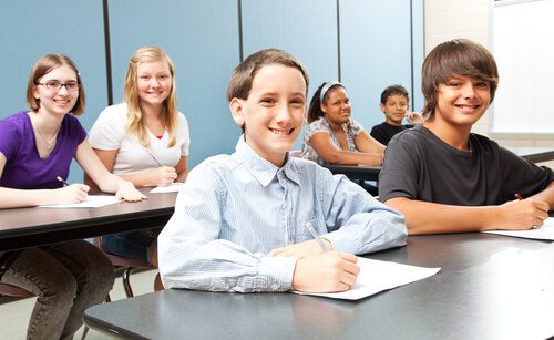 Children are smiling as they write on papers. These are middle school age children.