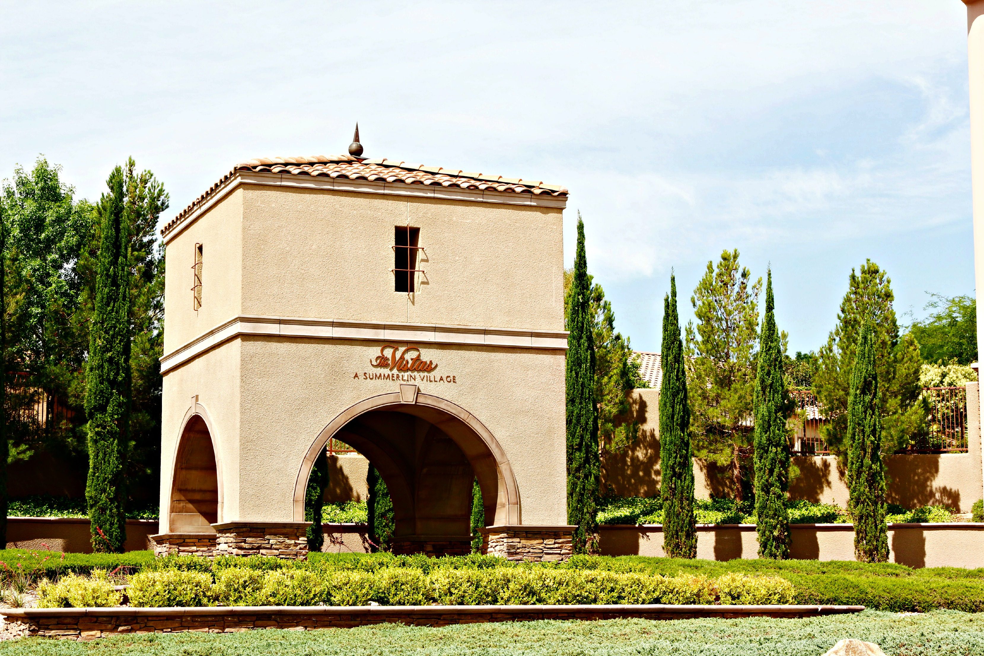 The Vistas Tower on the corner of the neighborhood against a blue sky and gree trees