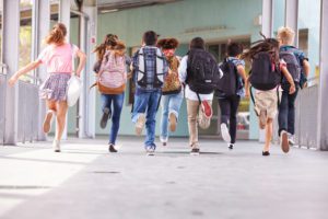 Middle School kids are running into school while wearing backpacks