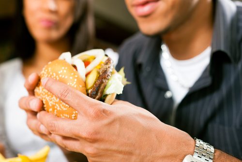 Man and Woman are sitting at a diner eating a well stacked hamburger