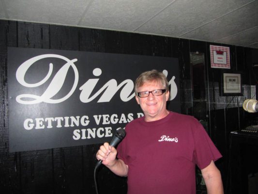 Host Danny G for karaoke is standing on stage with microphone in front of a banner that says Dino's getting Vegas Drunk 