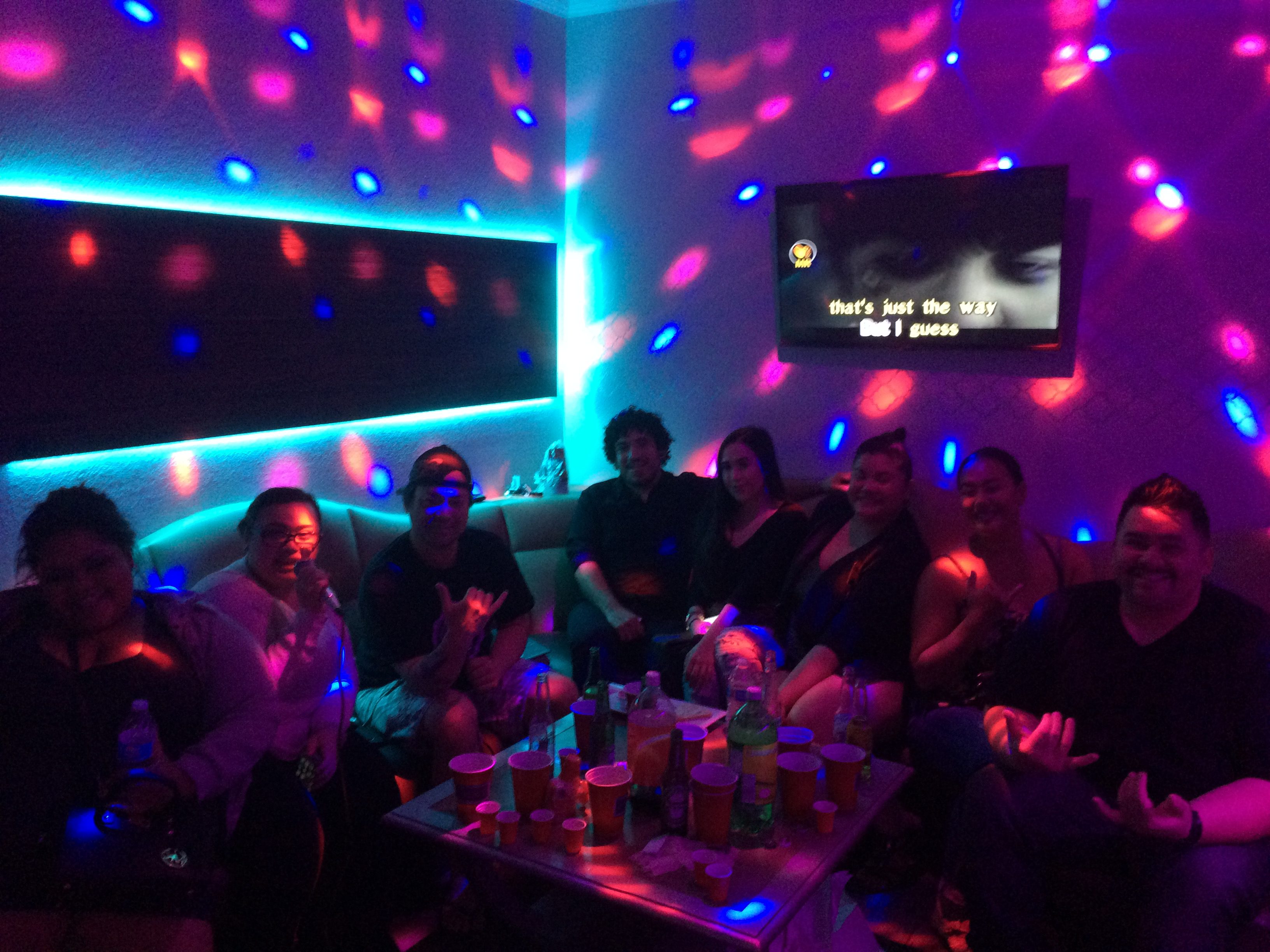 Go Go Karaoke room with group of people having fun at a party, sitting on the couch, karaoke monitor is showing words and someone is holding a microphone