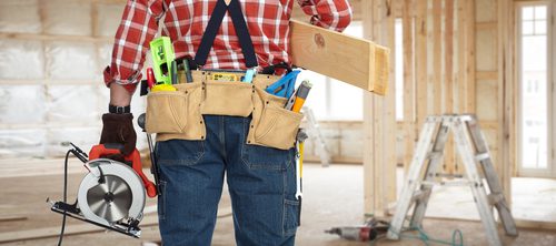 Man i sstanding in a home he's fixing up and is wearing a toolbelt