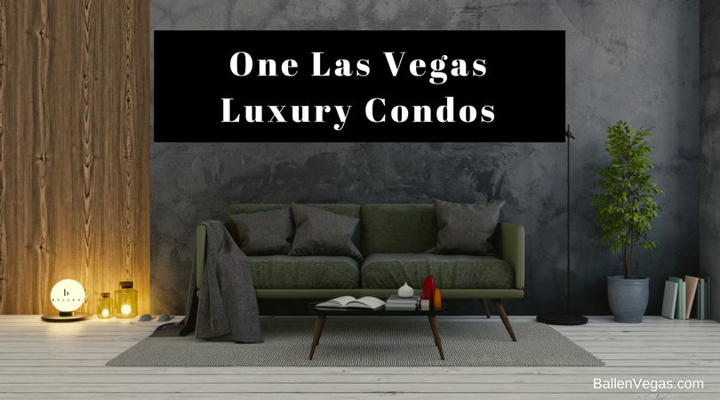 Grey Couch and dark wall with small table are in an open living room. Sign reads one las vegas luxury condos