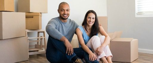 man and woman smiling as they sit among moving boxes