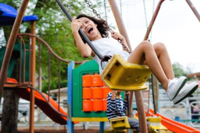 Child is swinging on a yellow swing at the park and smiling or laughing