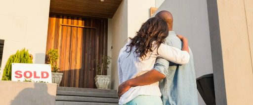 couple embracing with back to camera looking at sold home door