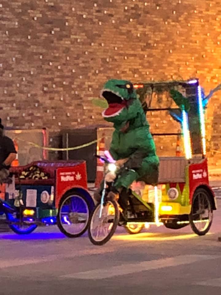 Pedi Cab driver is trying to get booked wearing a dinosaur costume.