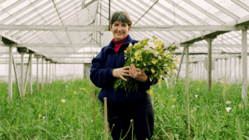 Woman is standing in a greenhouse holding flowers